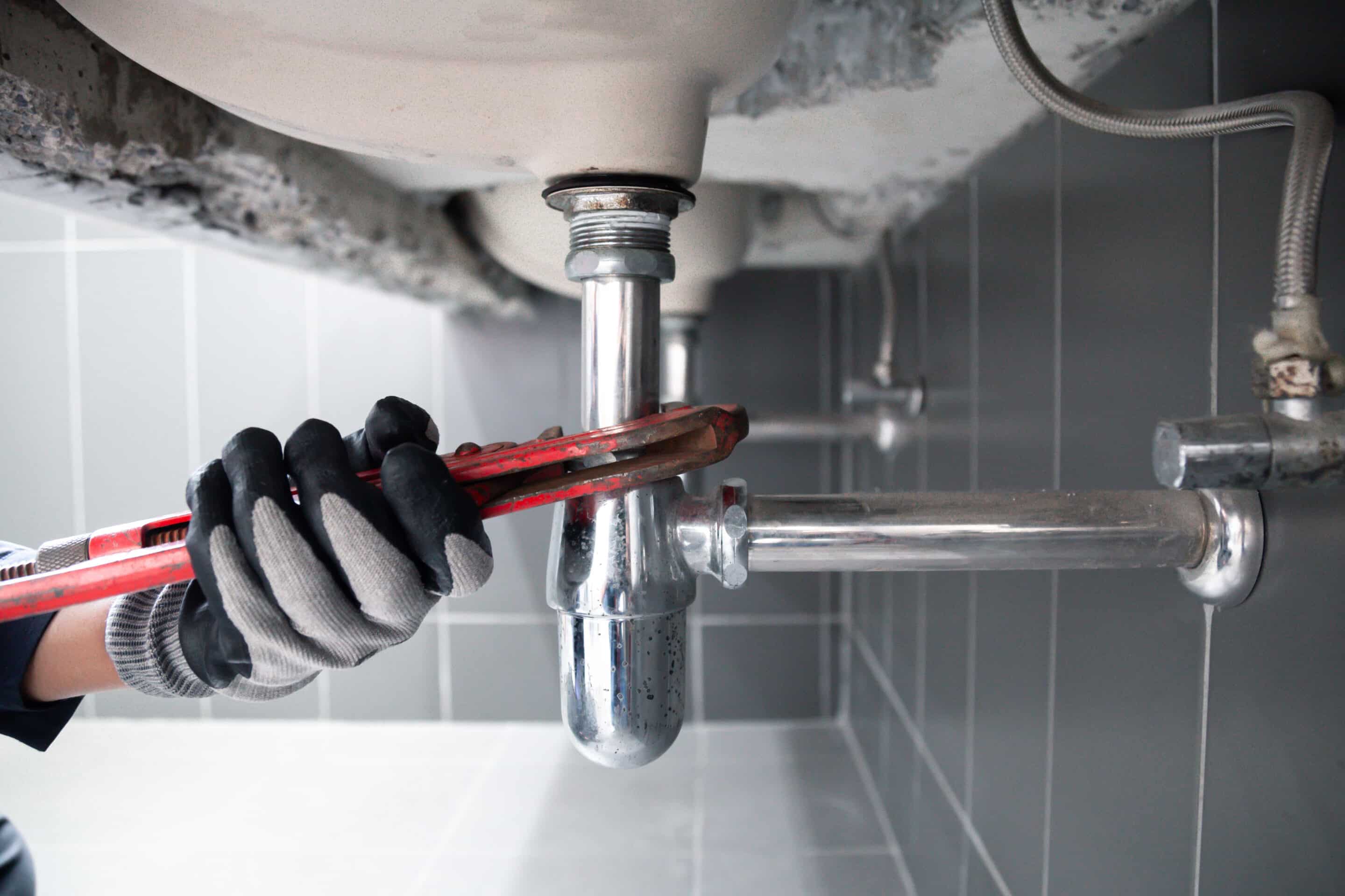 Plumber using a wrench to repair a water pipe under the sink. Concept of maintenance.specialist male plumber repairs faucet in bathroom. furnace repair image