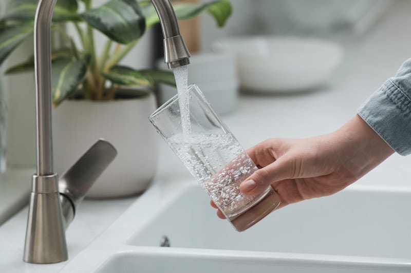 Woman filling glass with water from tap in kitchen, closeup water coming from kitchen faucet