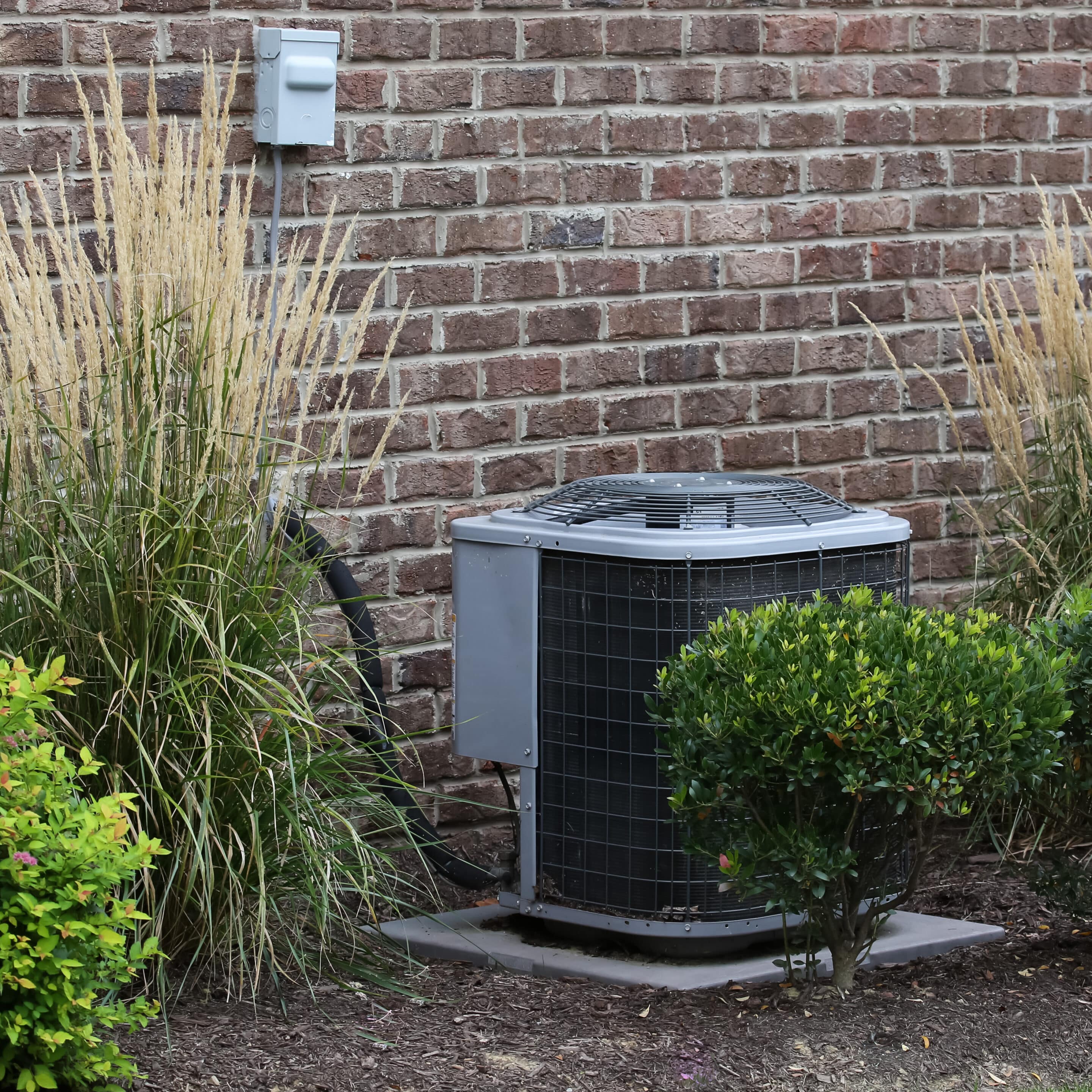 Air Conditioner Near House Surrounded By Shrubs